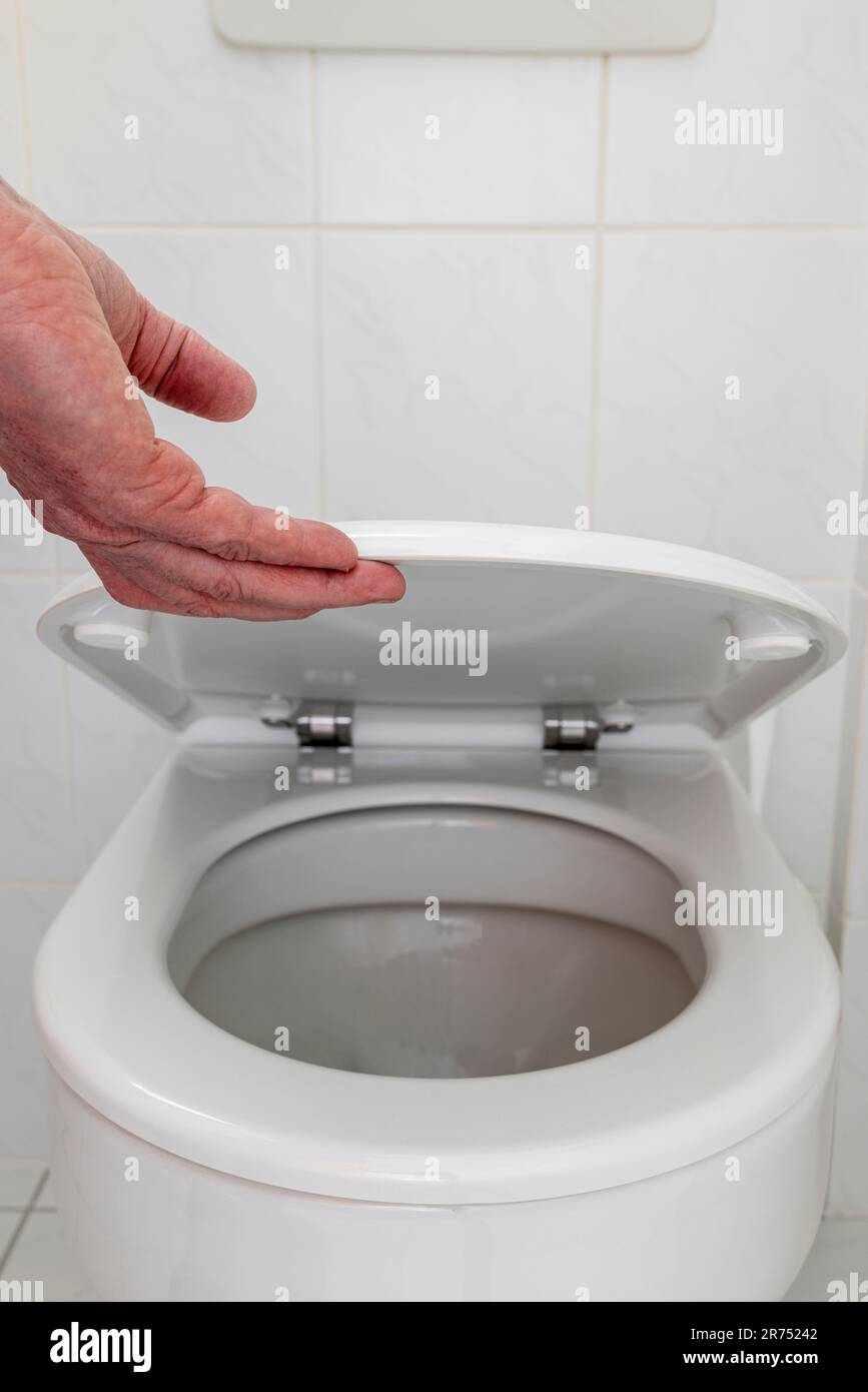 Man hebt mit der Hand den Toilettendeckel, den Toilettenspaziergang, Stockfoto