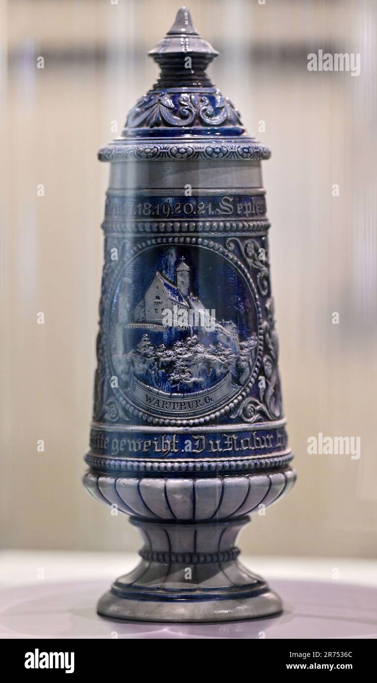 PRODUKTION - 12. Juni 2023, Thüringen, Eisenach: In der Wartburg-Ausstellung „Mythos Wartburg“ ist ein Becher mit Deckel und einem Bild der Wartburg zu sehen. Die Sonderausstellung "Wartburg-Mythos". 10 Questions to the Ideal Castle“ wird am 13. Juni eröffnet und bis zum 07. Januar 2024 ausgestellt. 1999 wurde die Wartburg als erstes und einziges Schloss Deutschlands von der UNESCO zum Weltkulturerbe erklärt. Mit der Ausstellung soll erforscht werden, warum die Wartburg so stark im öffentlichen Bewusstsein verankert ist und wie dieses reiche historische und kulturelle Erbe fortbestehen kann Stockfoto