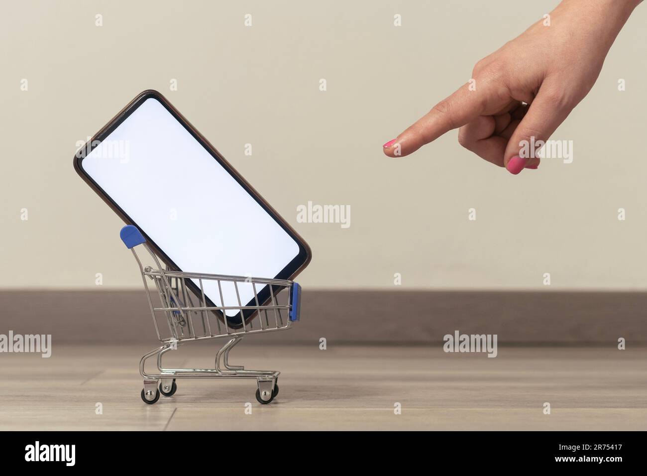 E-Commerce-Konzeptbild: Frau, die auf einen Wagen zeigt, mit einem Smartphone mit leerem Bildschirm Stockfoto