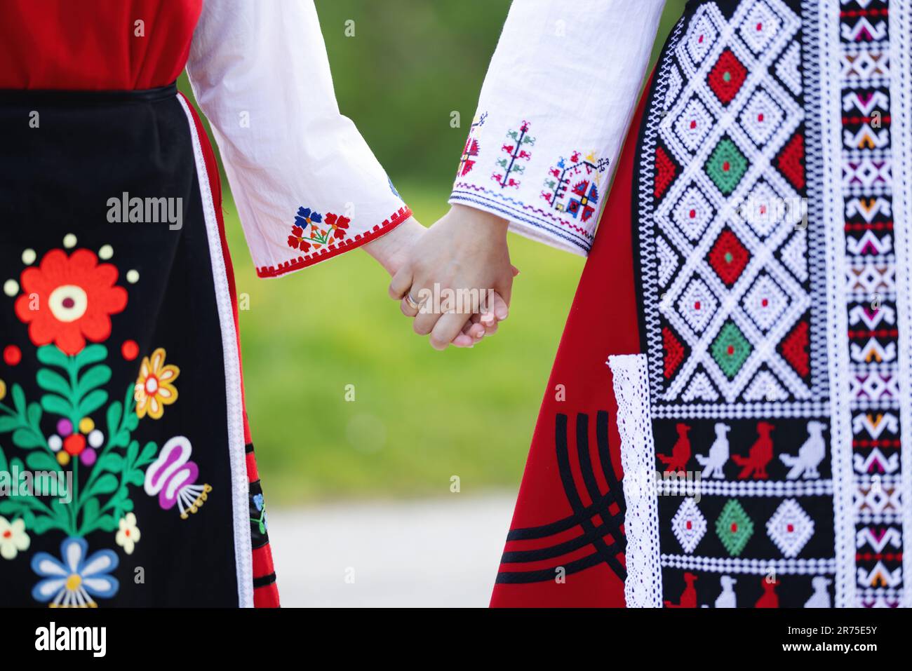 Mädchen in traditionellen bulgarischen ethnischen Kostümen mit folkloristischer Stickerei, die Händchen hält. Der Geist Bulgariens - Kultur, Geschichte und Traditionen. Stockfoto