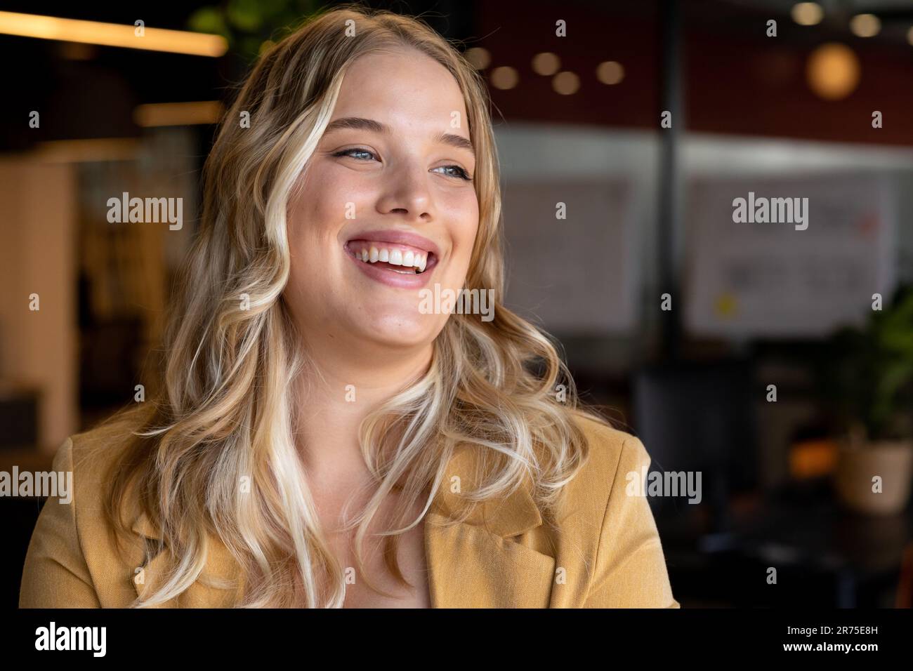 Glückliche weiße Geschäftsfrau in Übergröße mit langen blonden Haaren, die im Büro lächelt Stockfoto