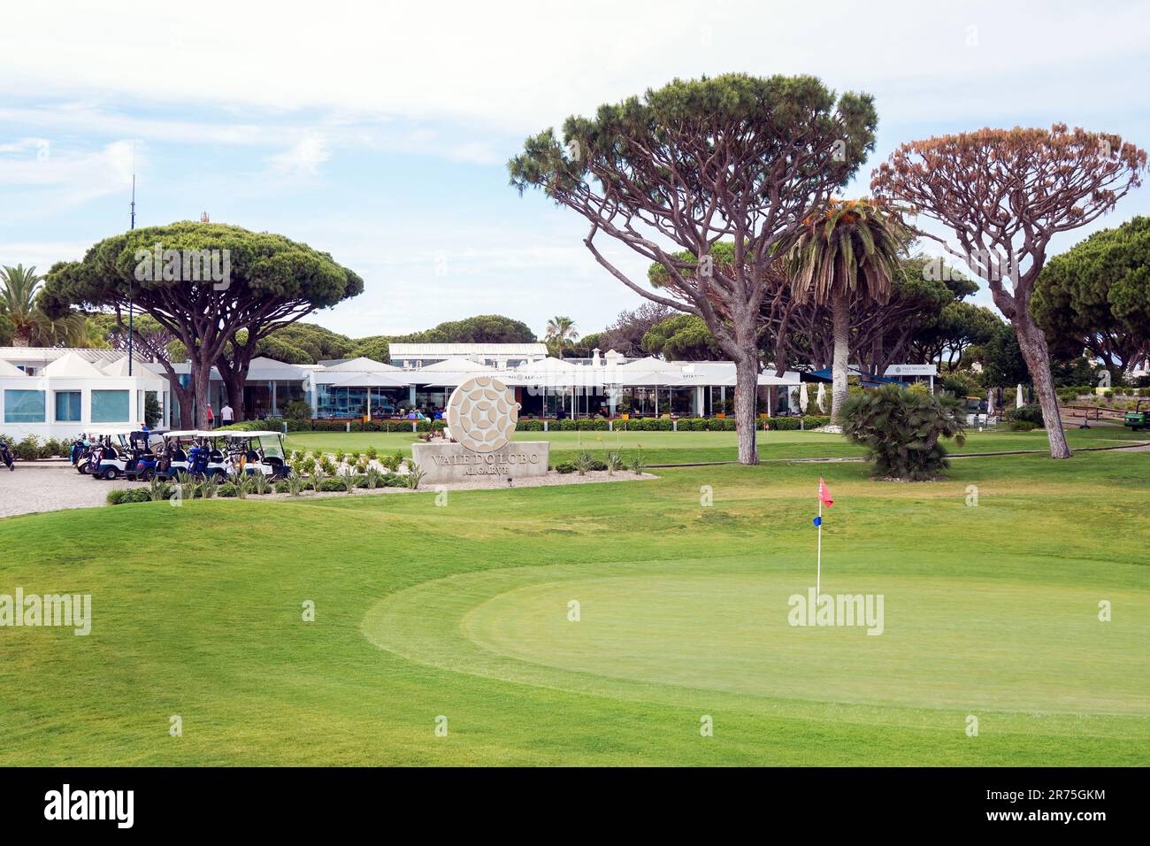 Begrüßungsschild am Golfklub und Golfplatz Vale do Lobo mit Golfbuggys und Golfschlägern und Blick auf das Clubhaus und Restaurant über dem 18. Stockfoto