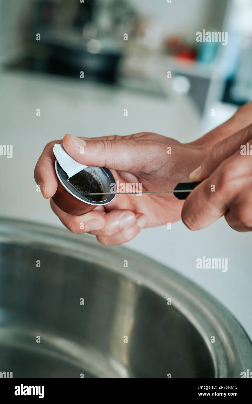 Ein Weißer benutzt ein Messer, um den gebrauchten gemahlenen Kaffee einer Kapsel zu entleeren, um ihn in den recycelbaren Mülleimer zu werfen Stockfoto