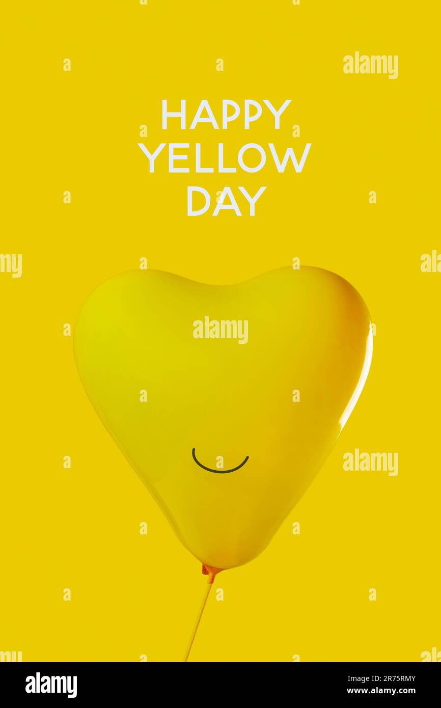 Ein aufgeblasener gelber, herzförmiger Ballon mit einem Lächeln und dem Text Happy Yellow Day auf gelbem Hintergrund Stockfoto