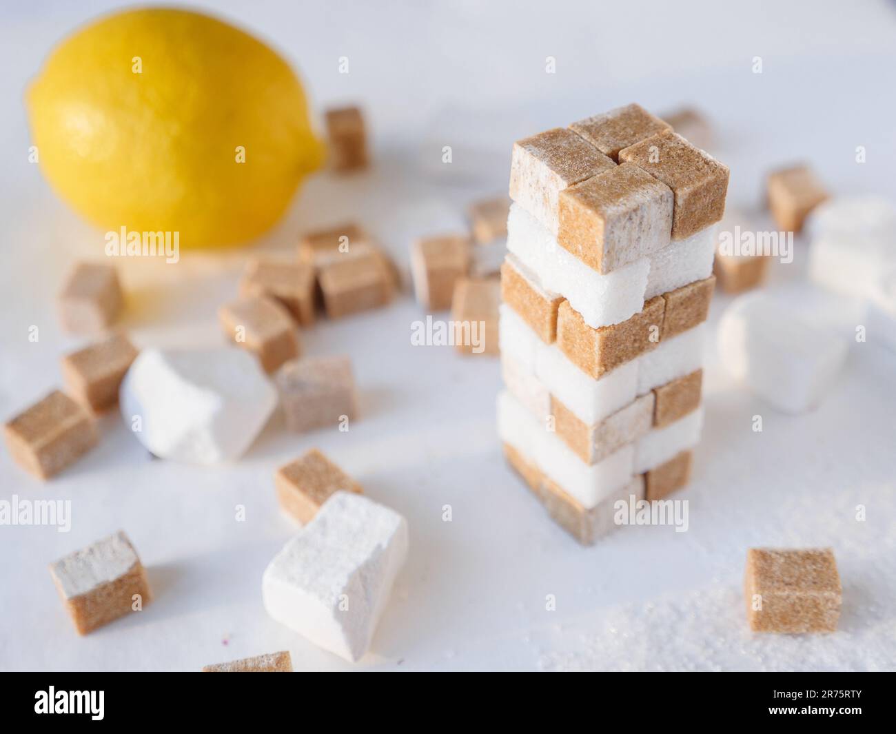 Ein Turm aus weißen und braunen Zuckerwürfeln und frischer Zitrone im Hintergrund. Konzept für süße und saure Speisen. Stockfoto