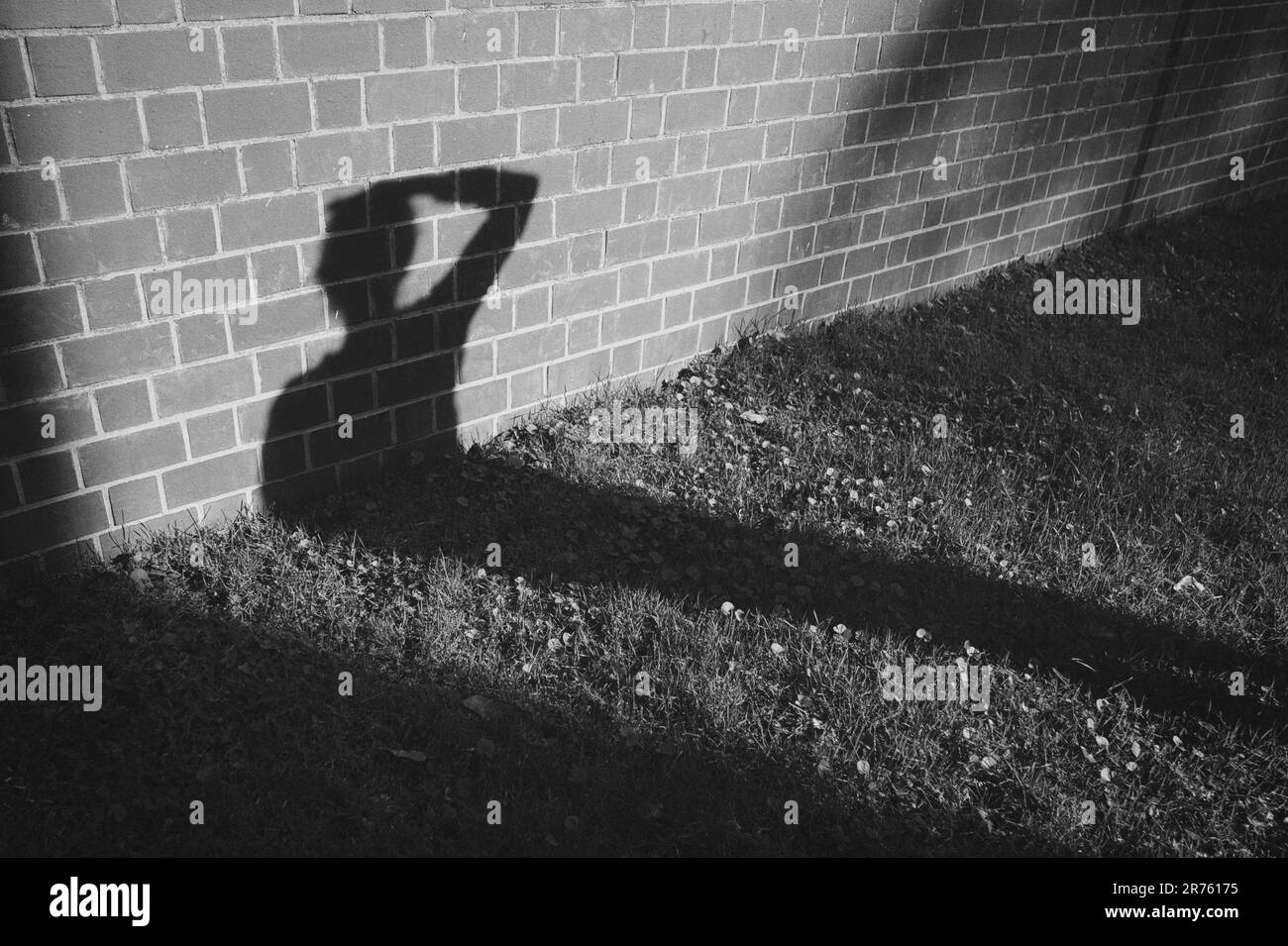 Die Silhouette einer menschlichen Figur sticht vor einer Backsteinwand hervor, die von einer Lichtquelle beleuchtet wird, die einen Schatten wirft Stockfoto