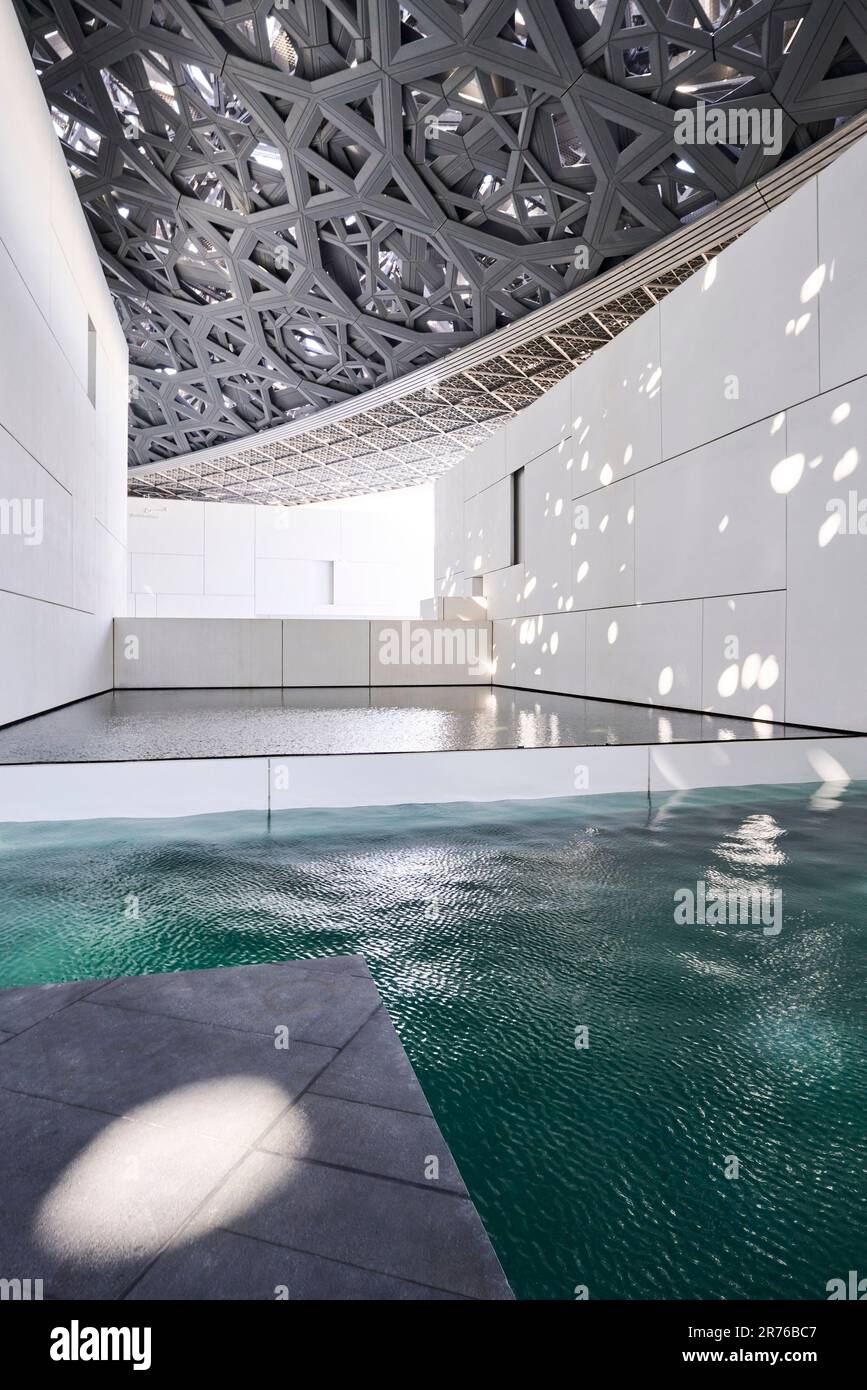 Innenraum mit Netzdach und Wasserelement. Louvre Abu Dhabi, Abu Dhabi, Vereinigte Arabische Emirate. Architekt: Jean Nouvel, 2017. Stockfoto