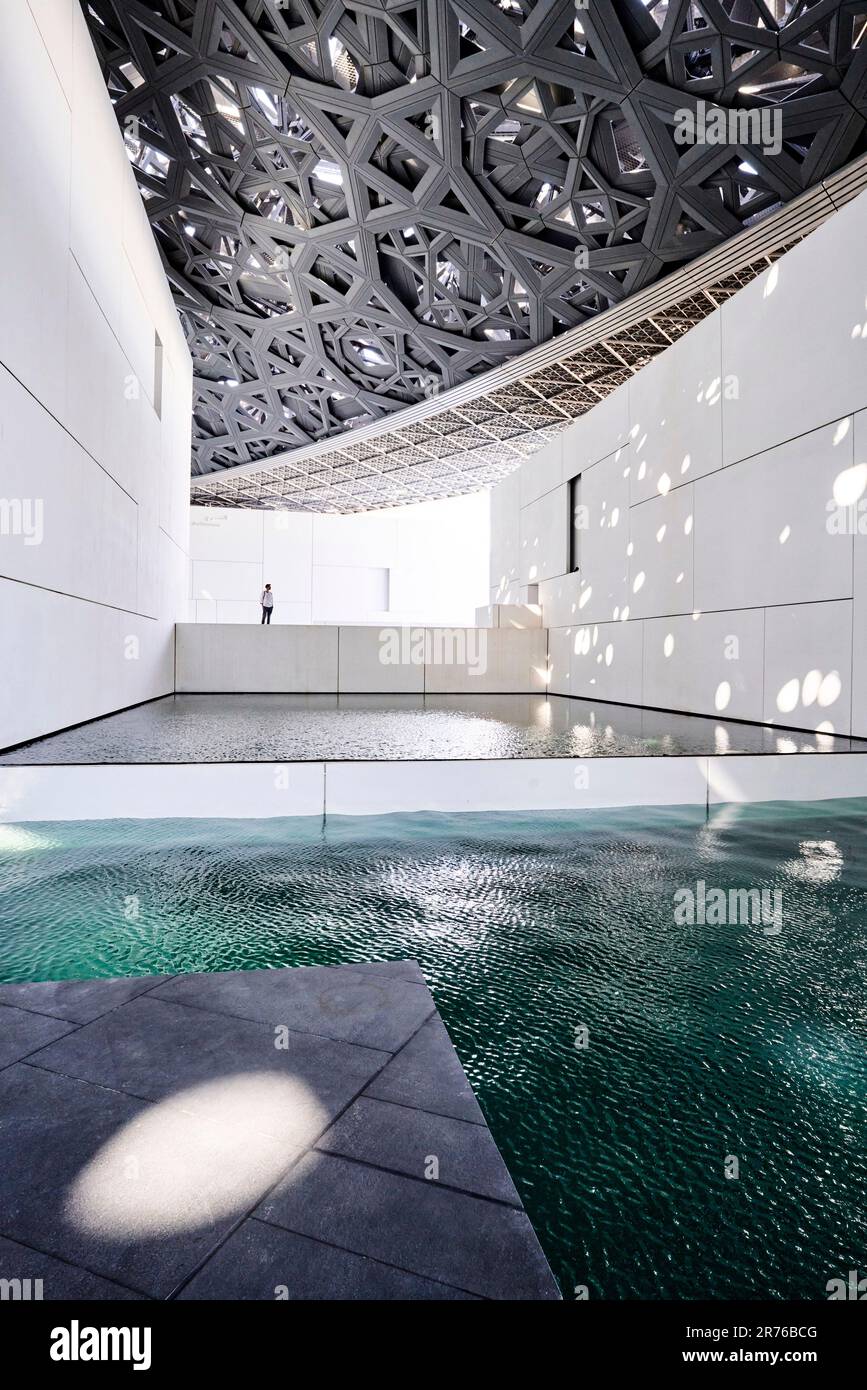 Innenraum mit Netzdach und Wasserelement. Louvre Abu Dhabi, Abu Dhabi, Vereinigte Arabische Emirate. Architekt: Jean Nouvel, 2017. Stockfoto