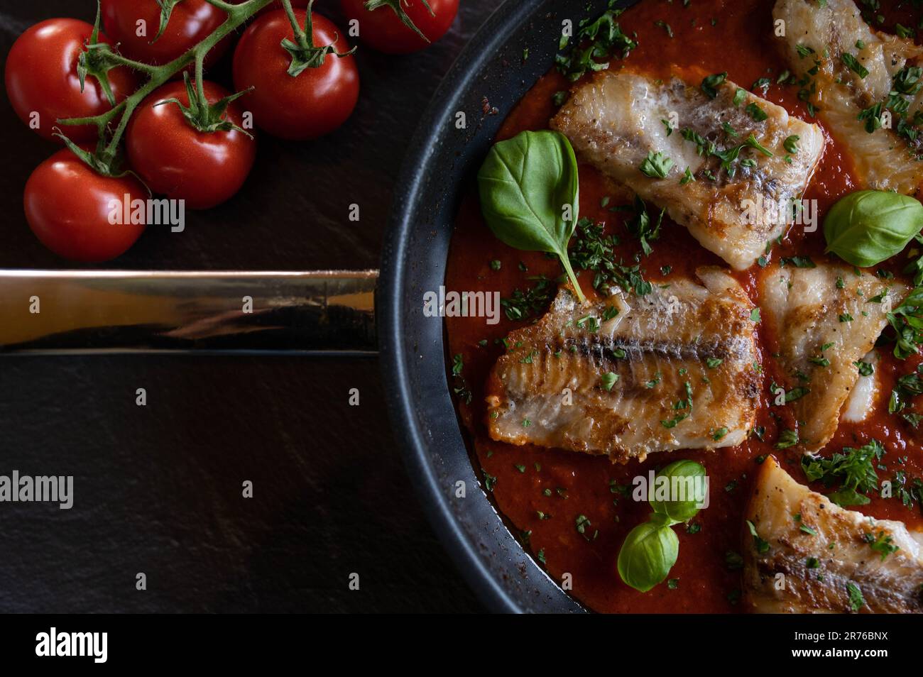 Gebratener Fisch in einer scharfen Tomatensoße auf dunklem Hintergrund. Schwache Beleuchtung Stockfoto