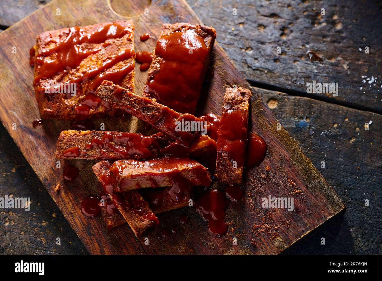 Blick von oben auf schmackhafte gegrillte Schweinerippchen mit Ketchup, serviert auf Holzbrett in der Küche Stockfoto