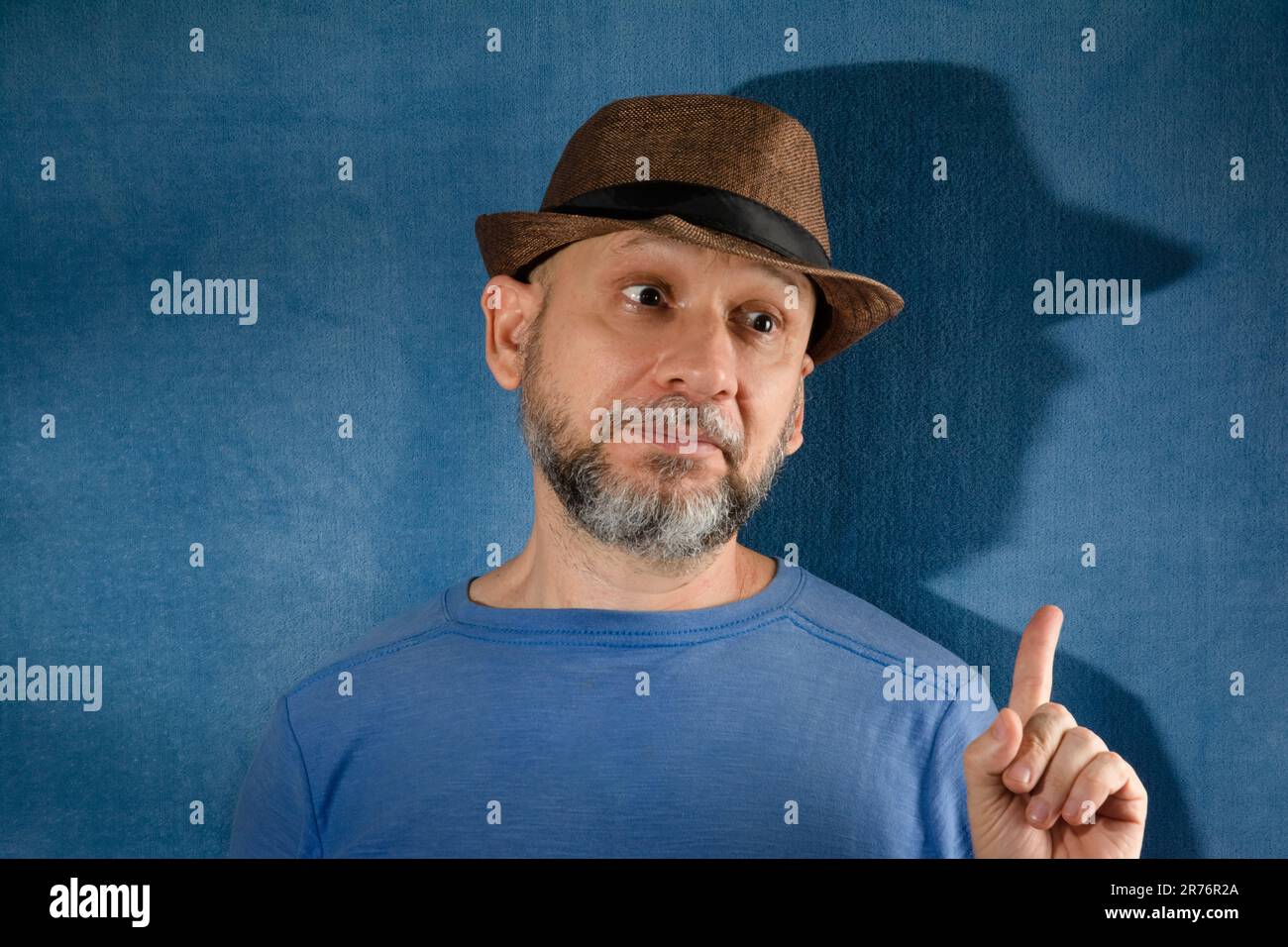 Ein Mann, der einen stilvollen schwarzen Fedora-Hut trägt, während er auf etwas mit einem entschlossenen Ausdruck zeigt Stockfoto