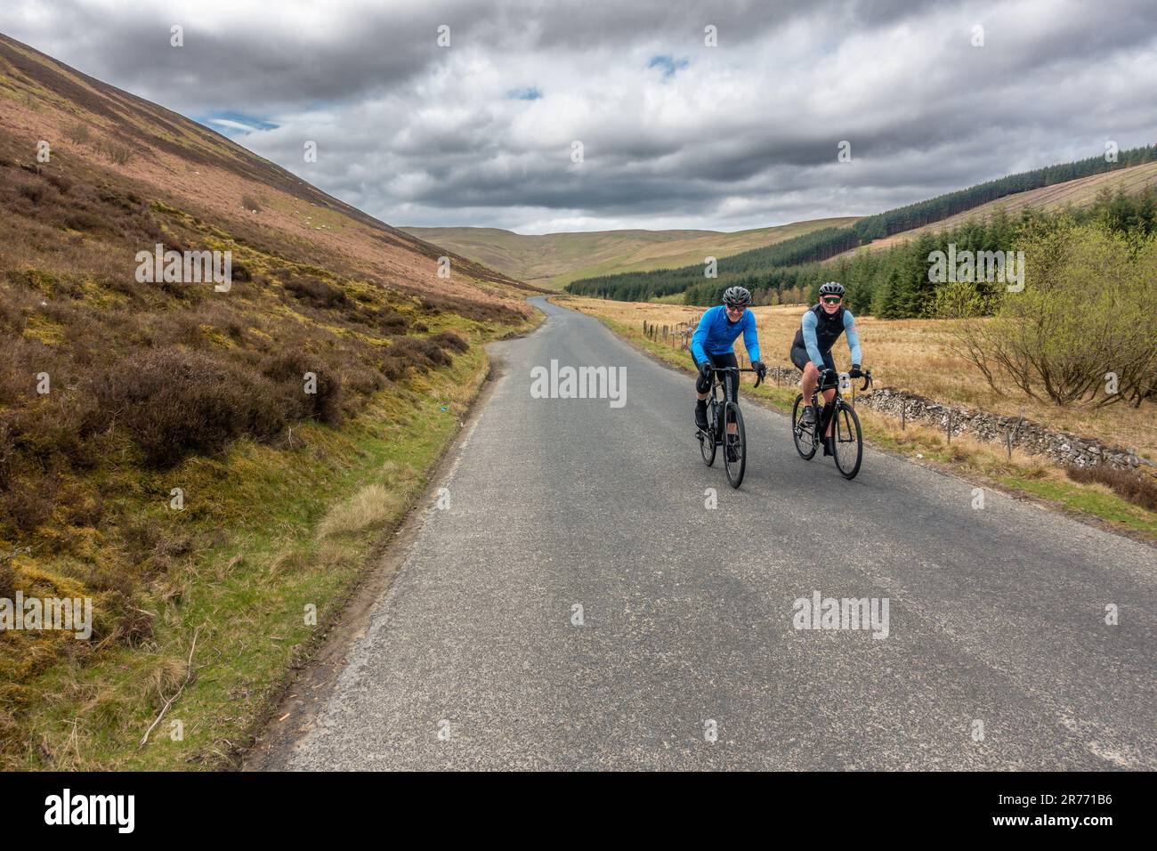 Zwei fröhliche Männer, die auf dem Road Bike auf der B709 durch wunderschöne Landschaften und ruhige Straßen fahren und sich fit halten an den schottischen Grenzen, Schottland, U Stockfoto