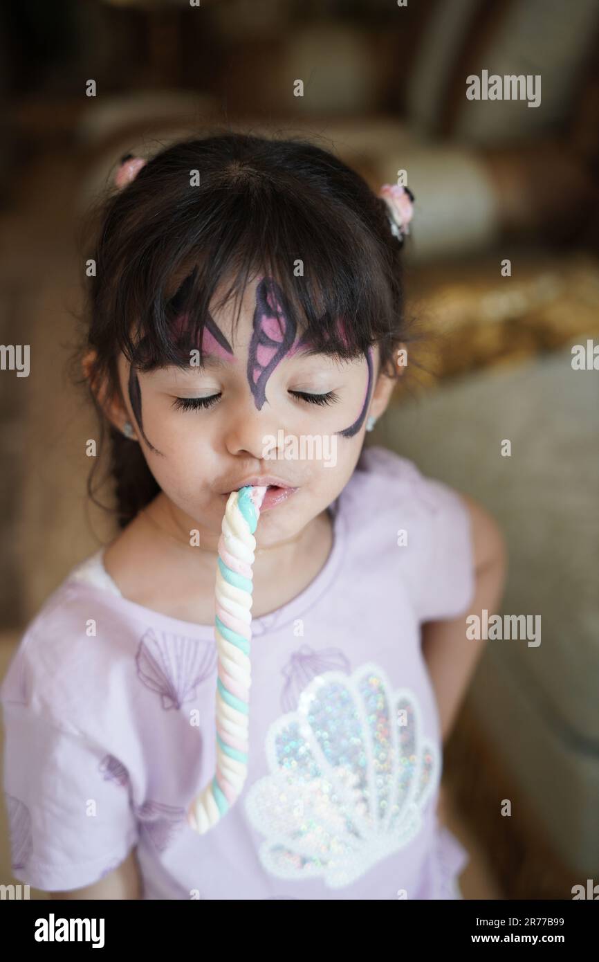 Unartige Kinderreaktion oder Gesichtsausdruck. Unartiges kleines Mädchen, das Süßigkeiten mit Gesichtsfarben isst. Stockfoto