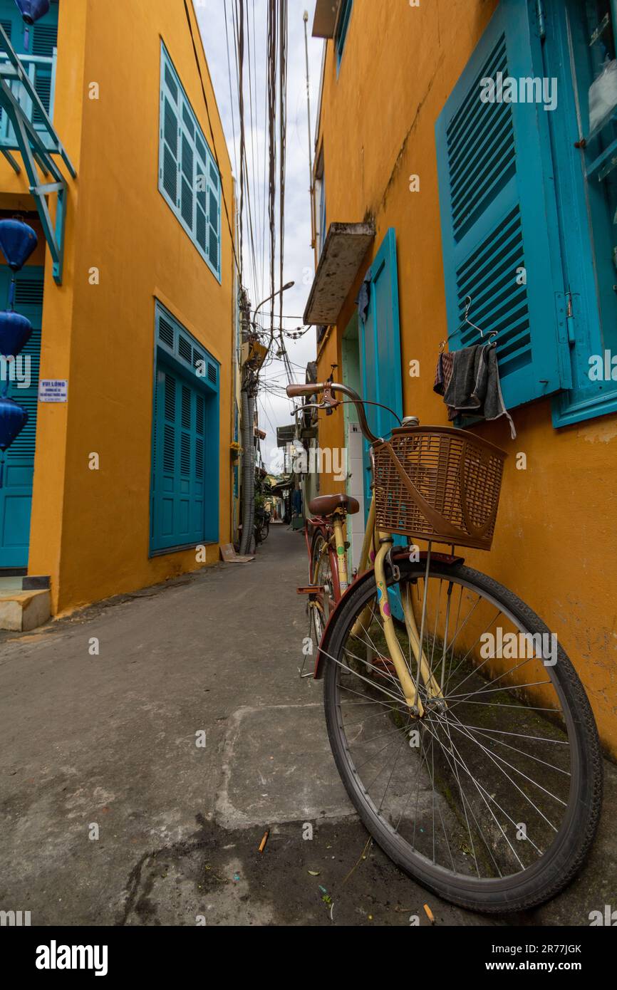 Ein altes Fahrrad steht in der engen Straße, umgeben von gelben Gebäuden mit blauen Fenstern und Türen. Altstadt von Hoi an, Vietnam. Stockfoto