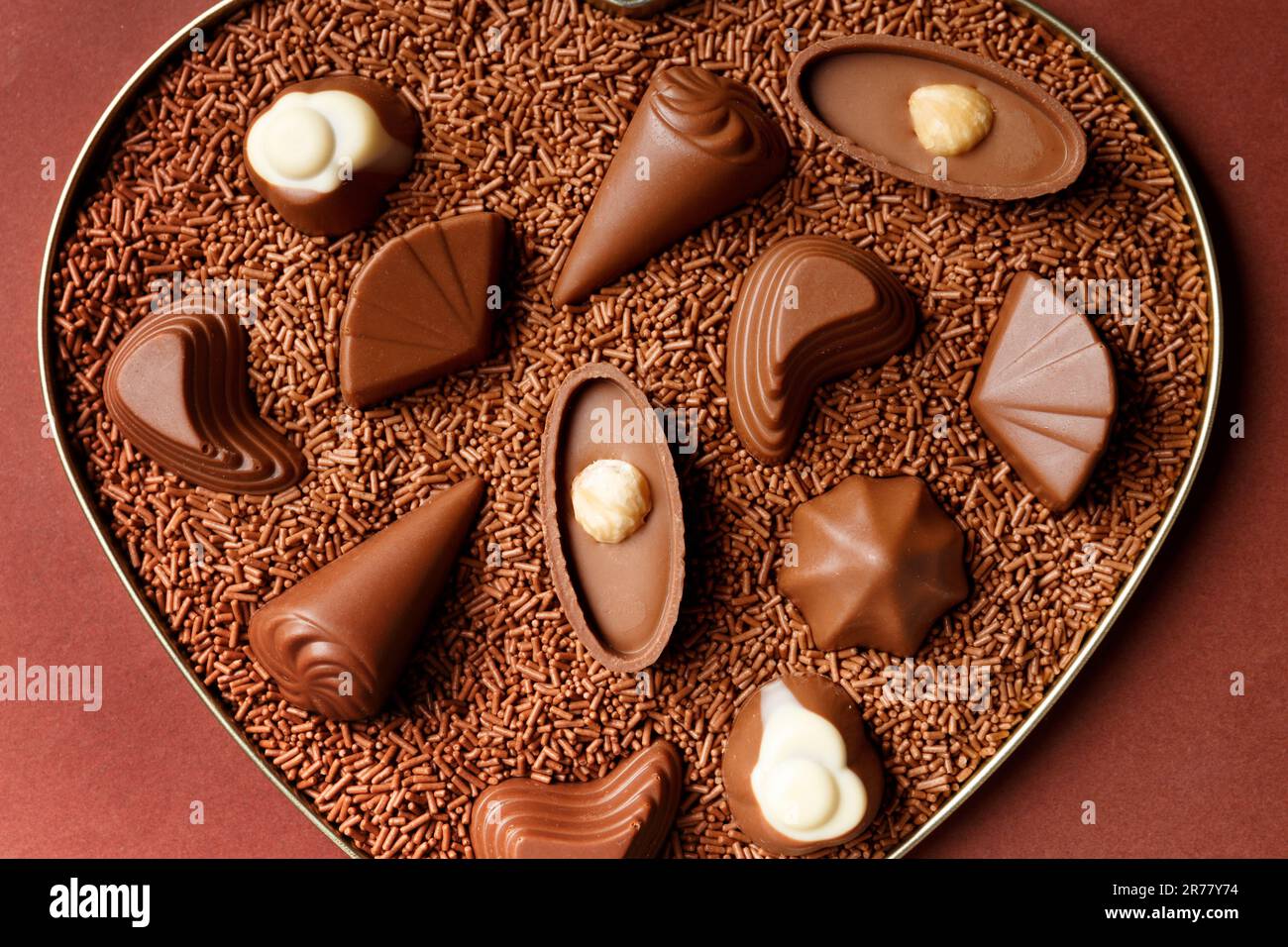 Schokoladenbonbons in Schokoladenstückchen in einer Herzbox auf braunem Hintergrund, aus nächster Nähe, Valentinstag. Stockfoto