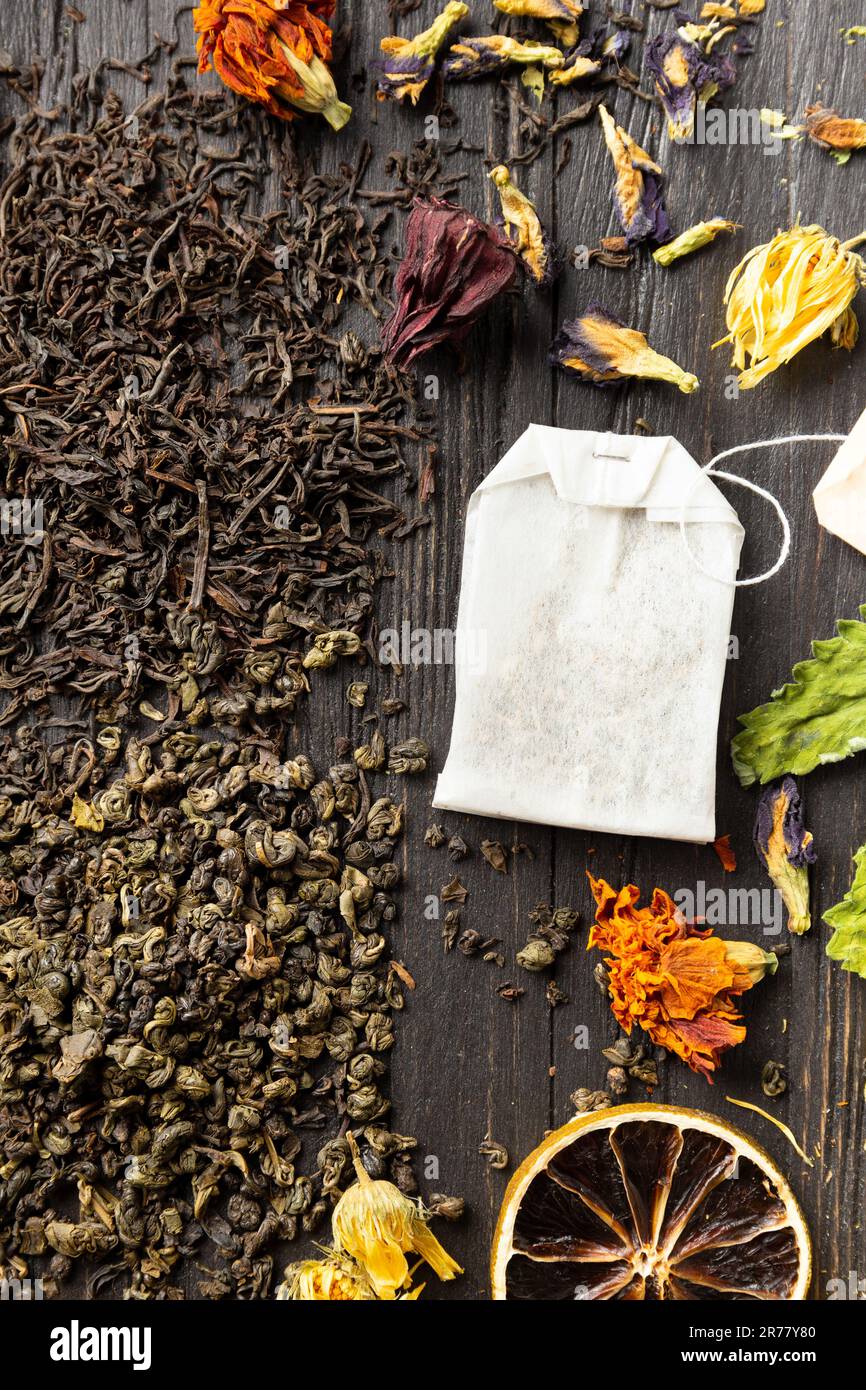 Zusammensetzung von trockenem schwarzen und grünen Tee, Teebeutel, getrockneten Zitrusscheiben und trockenen Hibiskusblumen auf dunklem Holzhintergrund von oben. Verschiedene Arten von Stockfoto