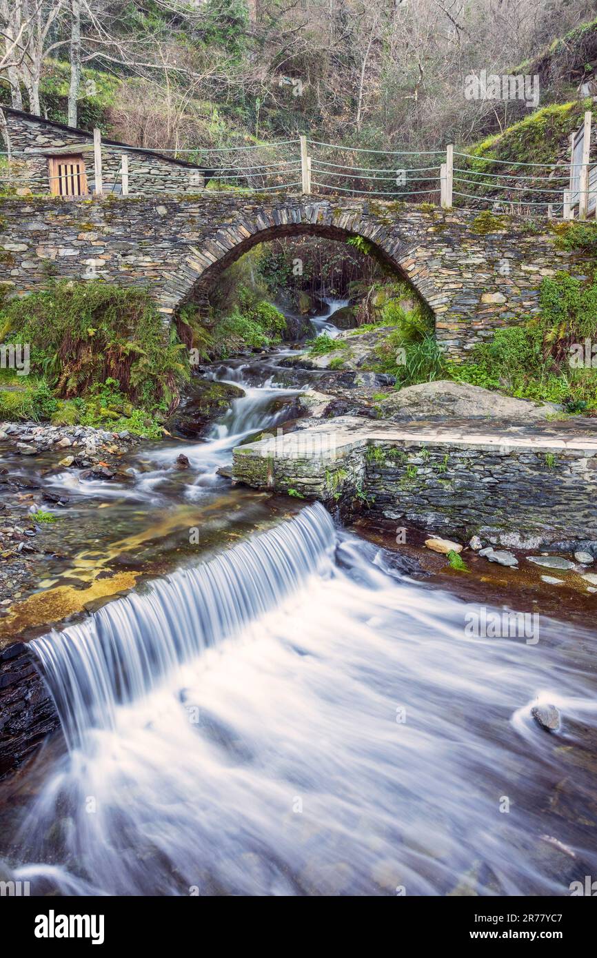 Blick auf den Wasserfall und die Steinbrücke über einen Bach am Flussstrand des historischen Dorfes Piódão in Portugal. Stockfoto