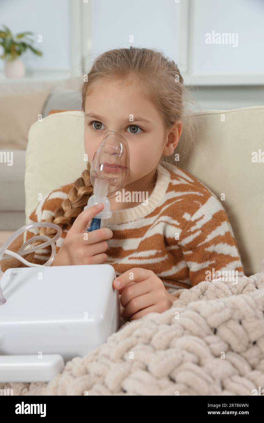 Kleines Mädchen mit Vernebler zur Inhalation im Sessel zu Hause Stockfoto