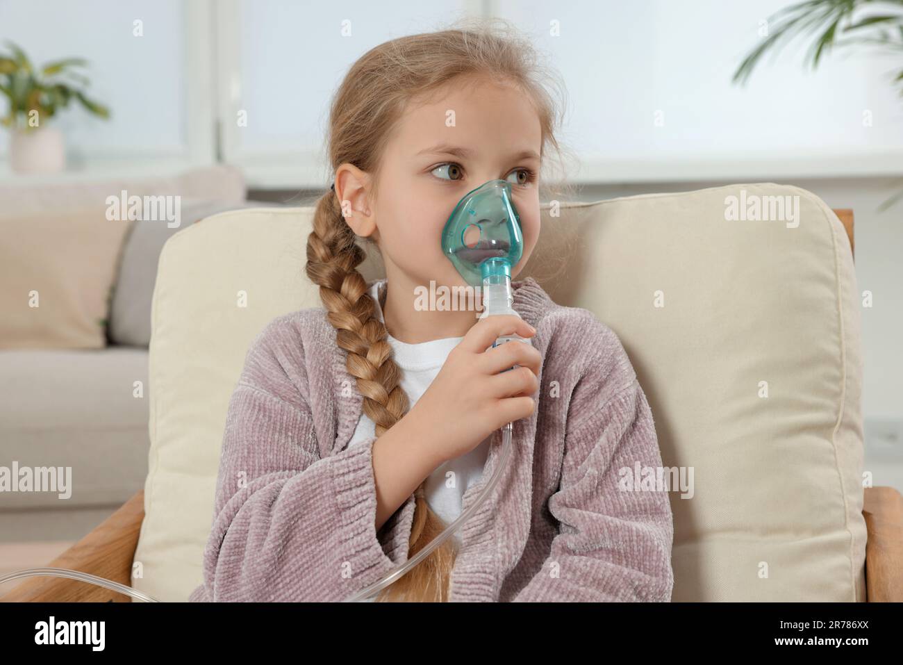 Kleines Mädchen mit Vernebler zur Inhalation im Sessel zu Hause Stockfoto