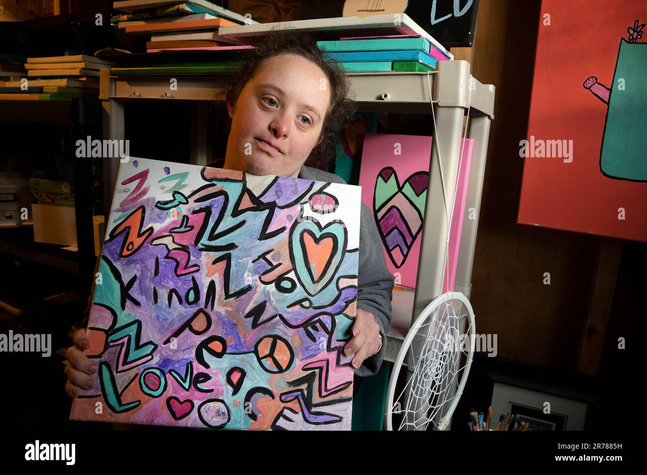 Raleigh, North Carolina, USA. 12. Dezember 2022. Caroline Dempsey, 26, die aufgrund des Down-Syndroms eine Entwicklungsbehinderung hat, lässt nicht zu, dass ihre Herausforderung sie von ihrer Liebe zu Natur und Kunst abhält. Die junge Künstlerin konnte eine Reihe ihrer Gemälde verkaufen und hofft, dass sie mit wachsendem Interesse an Folk Art mehr verkaufen kann. Abbildung: Caroline in ihrem Raleigh, NC-Kellerstudio mit einem aktuellen Gemälde (Kreditbild: © Robin Rayne/ZUMA Press Wire), NUR REDAKTIONELLE VERWENDUNG! Nicht für den kommerziellen GEBRAUCH! Stockfoto