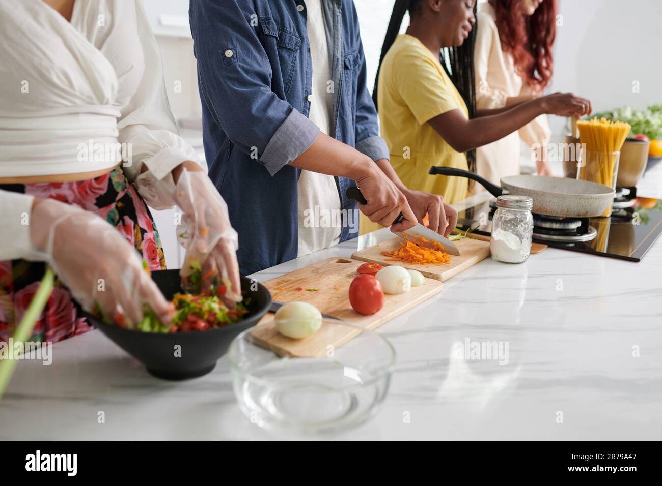 Kurze Aufnahme von jungen interkulturellen Freunden in Freizeitkleidung, die zusammen Essen in der Küche kochen, während einer von ihnen frische Karotten hackt Stockfoto