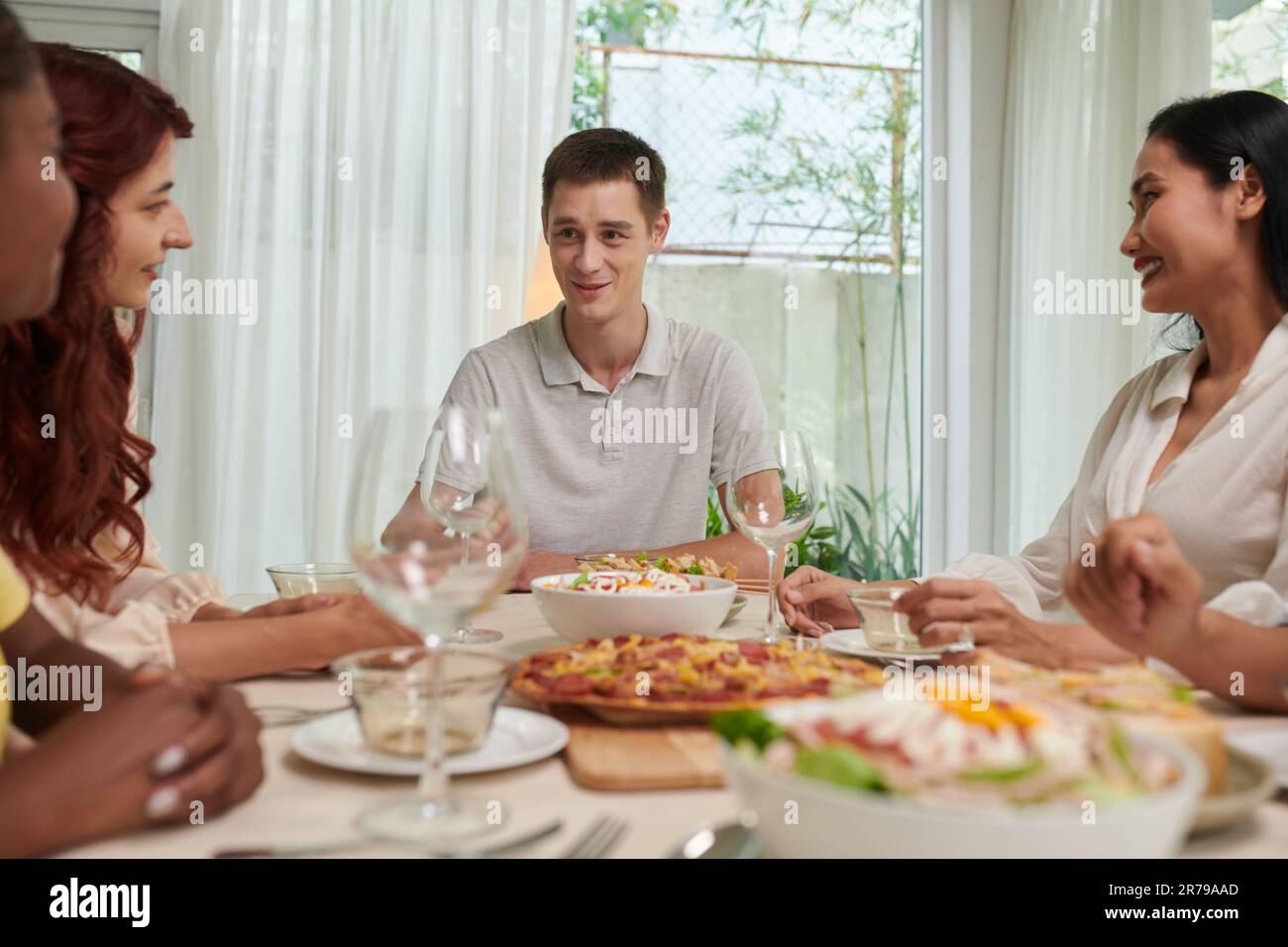Konzentrieren Sie sich darauf, den jungen Mann in legerer Kleidung zu lächeln, sitzen Sie am Tisch und genießen Sie zum Abendessen oder zur Feier hausgemachte Speisen, und sprechen Sie mit seinen Freunden Stockfoto