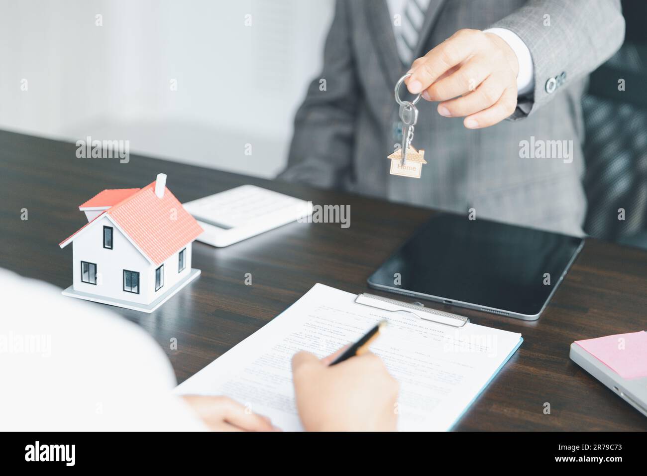 Hausverkaufs- und Hausversicherungskonzept. Immobilienmakler, der Frau Hausschlüssel übergibt und den Kunden bittet, die Dokumente zu unterzeichnen, um den Vertrag rechtmäßig zu machen Stockfoto