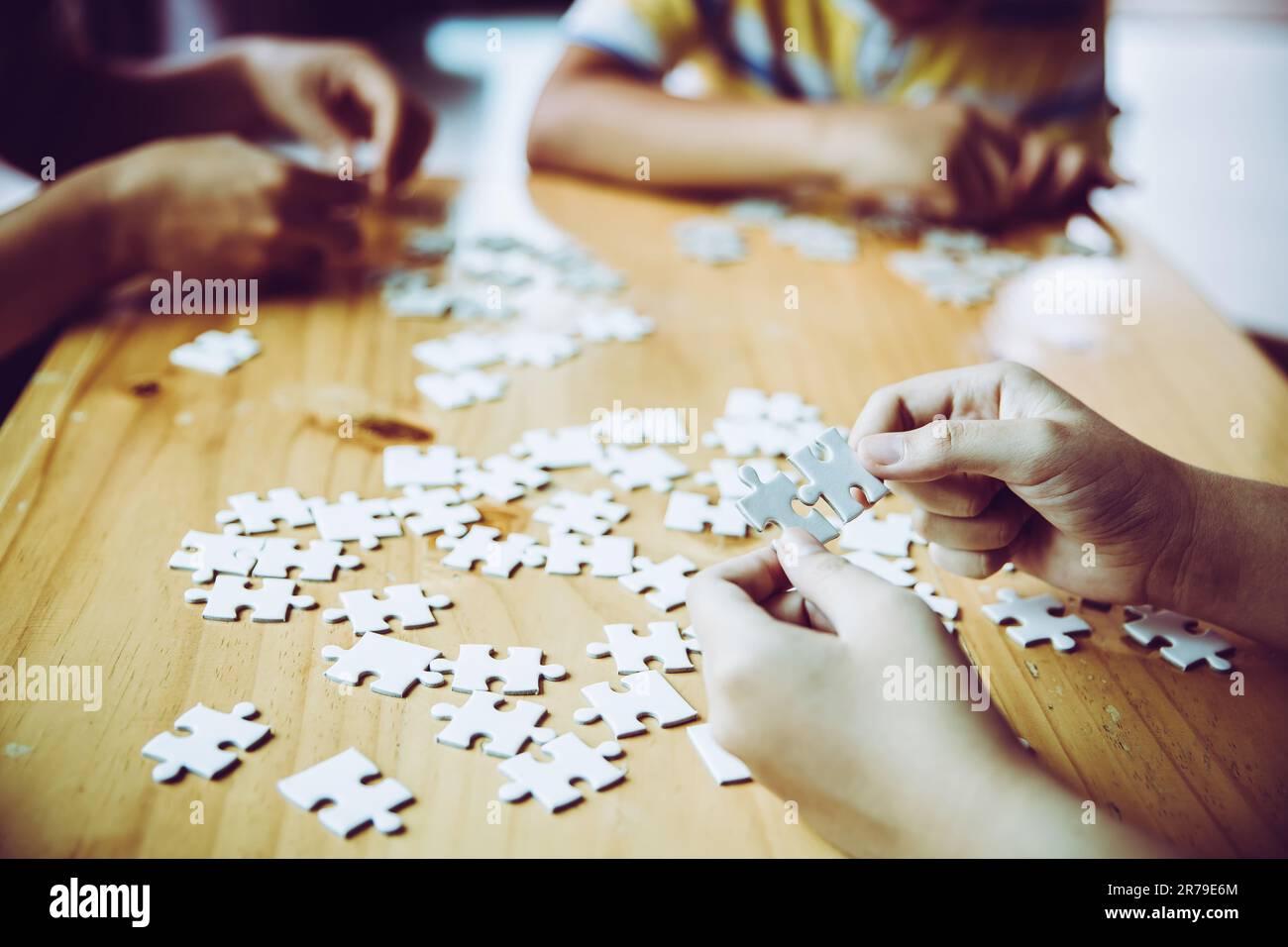 Die Hände eines kleinen Kindes und eines Elternteils, die zu Hause Puzzleteile spielen, zusammen auf einem Holztisch, Konzept für die Freizeit mit der Familie, spielen mit Witz Stockfoto