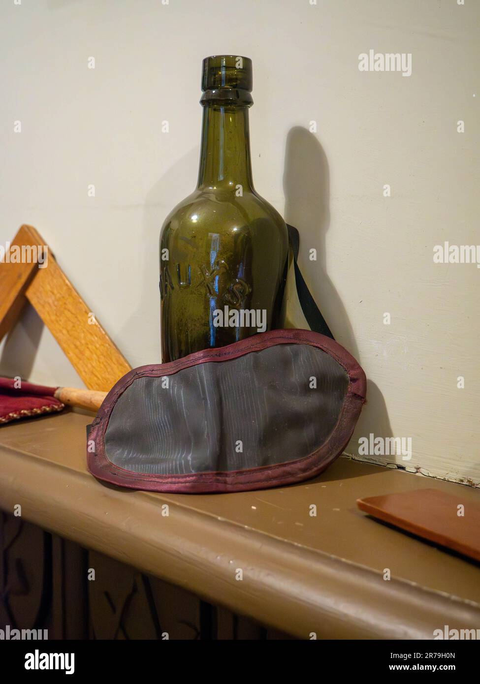 Eine grüne Glasflasche mit einer Augenmaske, die in der Freimaurerhalle im Beamish Museum, Stanley, County Durham, Großbritannien, auf einem Kaminsims hinterlegt wurde Stockfoto