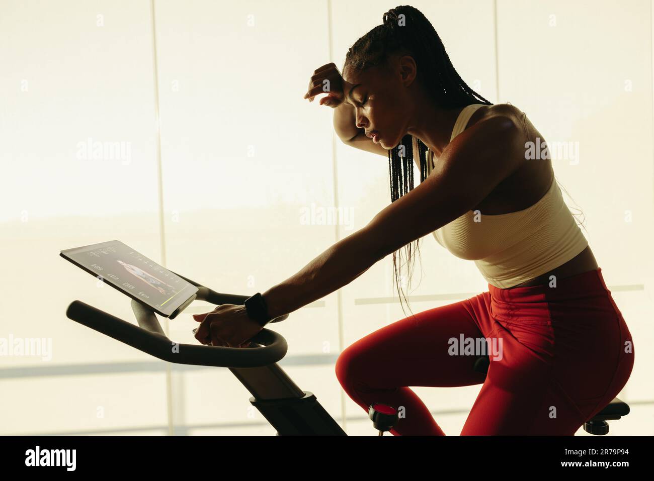 Eine junge schwarze Frau schwitzt mit einer Radfahrer-App. Mit ihrem Tablet in der Nähe folgt sie dem Online-Workout und schiebt Hersel Stockfoto