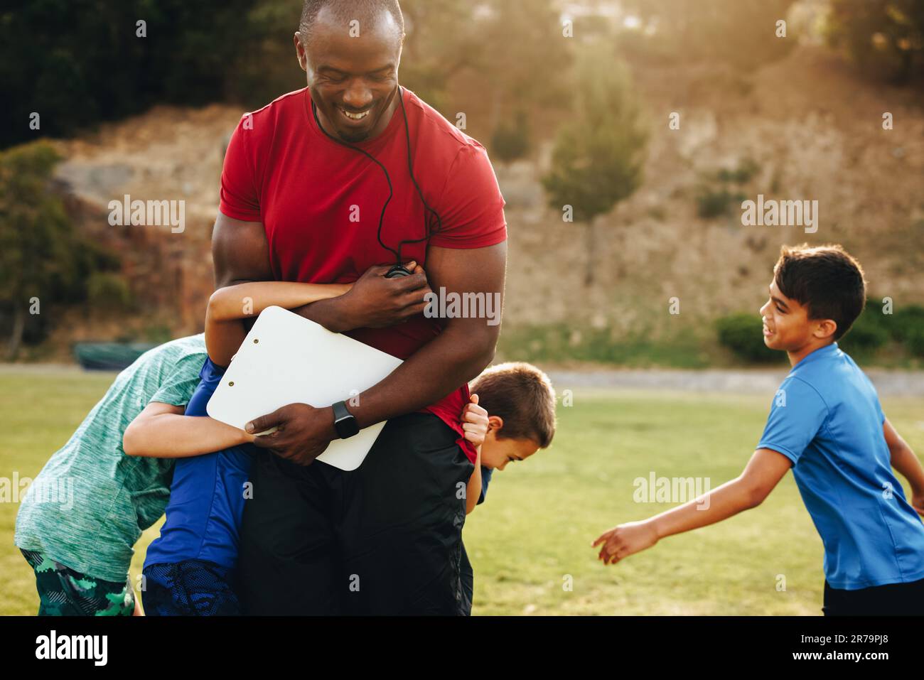 Kinder, die während eines Schultrainings mit ihrem Trainer spielen. Grundschüler, die Spaß an einem Sportunterricht haben. Sporttraini Stockfoto