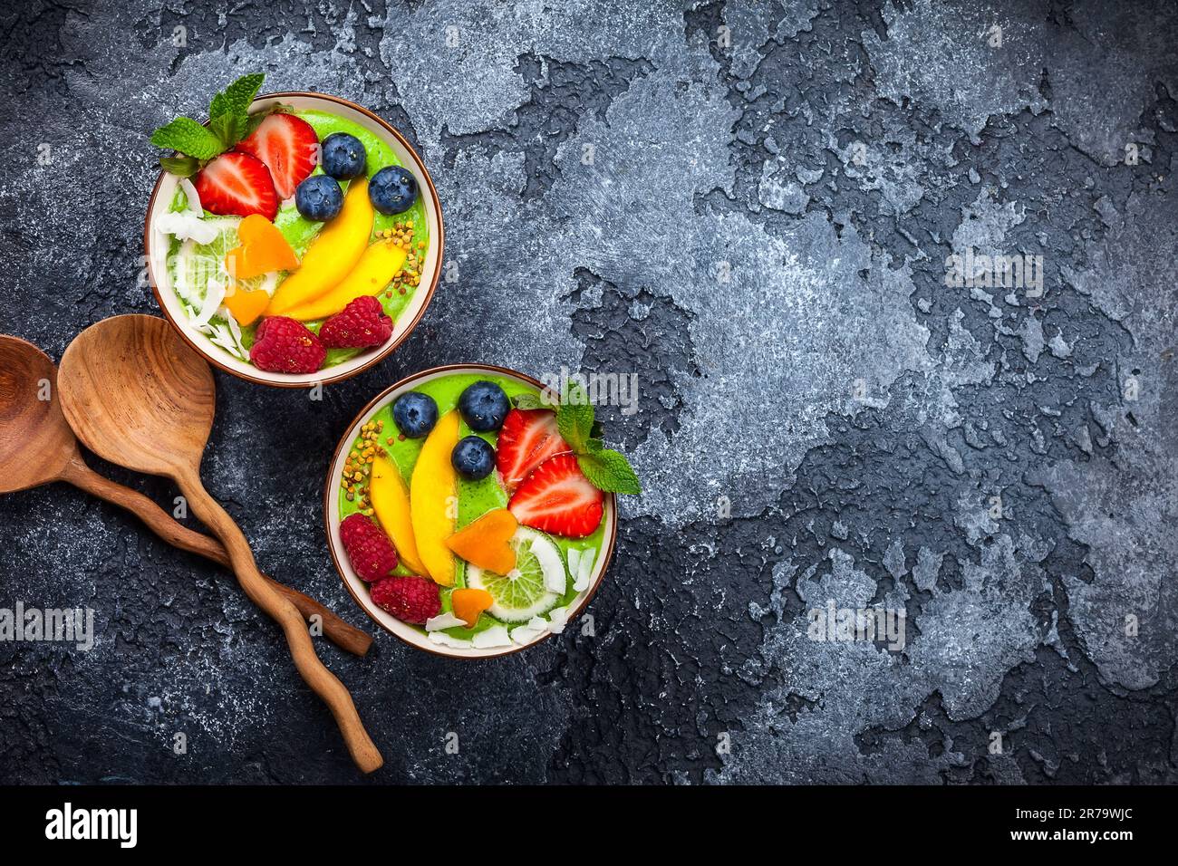 Grüner Smoothie in Schüsseln für gesundes Frühstück. Frischer Bio-Smoothie aus Spinat, Banane, Spirulina, Weizengras und Limette mit Beeren und Obst Stockfoto