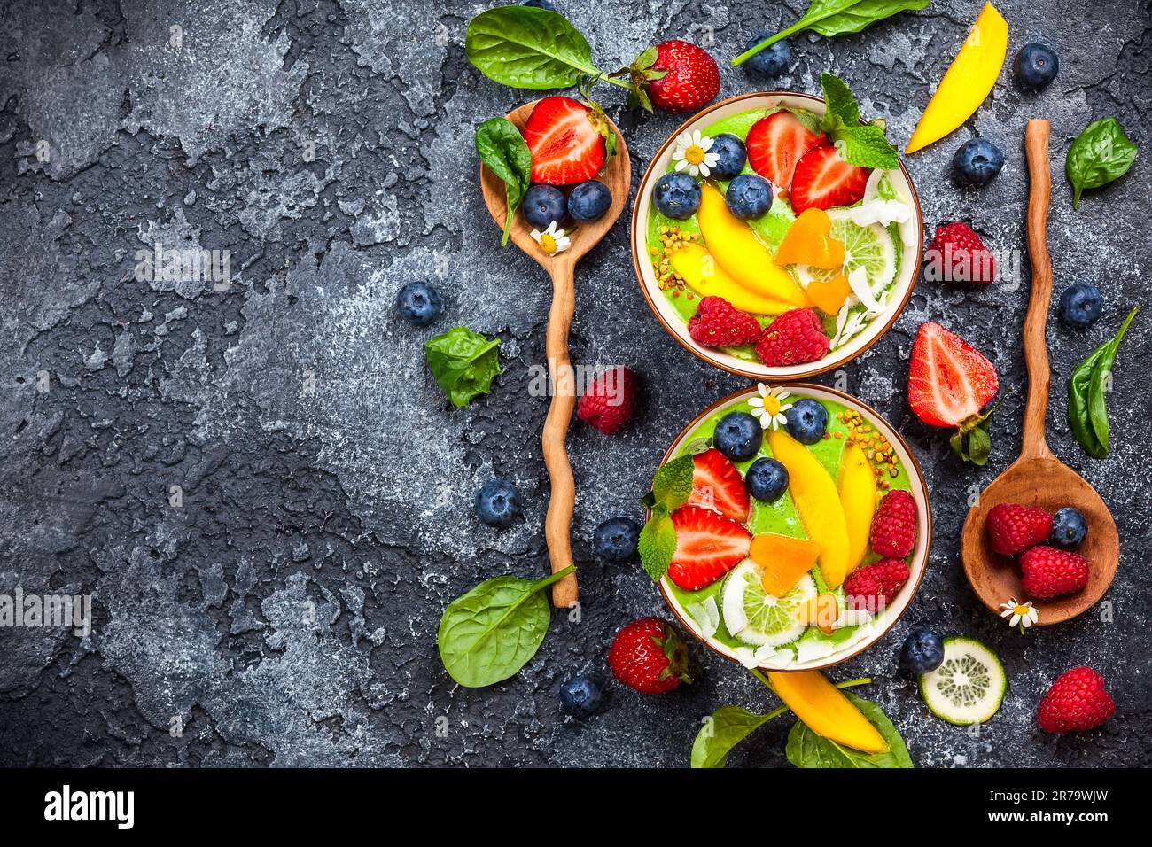 Grüner Smoothie in Schüsseln für gesundes Frühstück. Frischer Bio-Smoothie aus Spinat, Banane, Spirulina, Weizengras und Limette mit Beeren und Obst Stockfoto