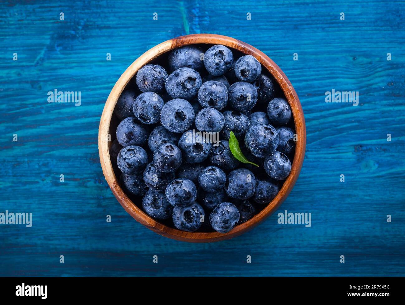 Frische Heidelbeere mit Wassertropfen in Holzschüssel auf blauem Hintergrund. Draufsicht. Konzept der gesunden und Diät Essen Stockfoto