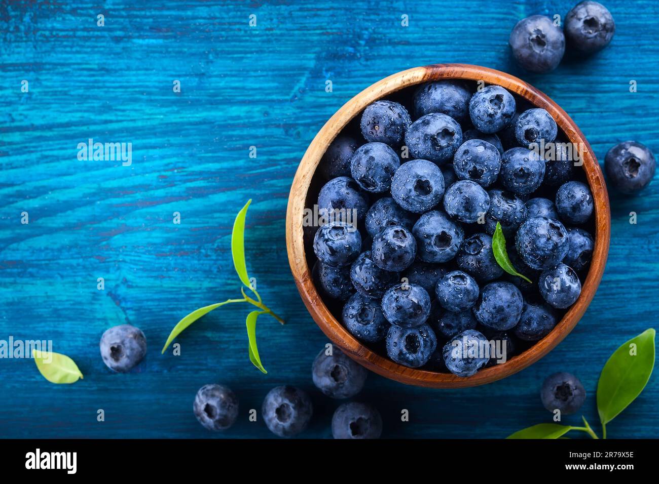 Frische Heidelbeere mit Wassertropfen in Holzschüssel auf blauem Hintergrund. Draufsicht. Konzept der gesunden und Diät Essen Stockfoto
