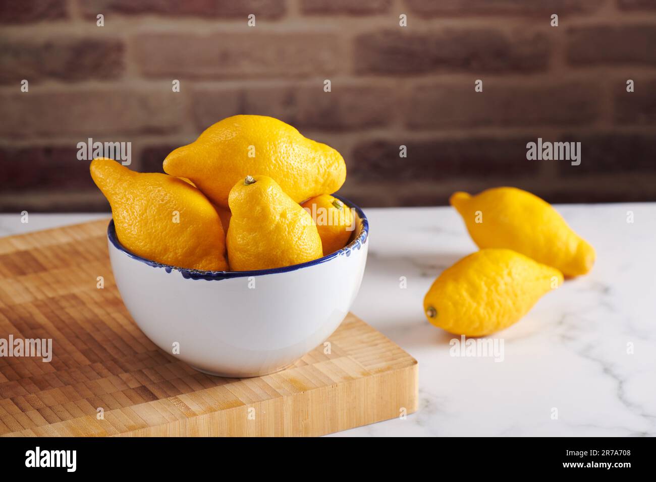 Zitronen in der Schüssel auf dem Schneidebrett auf der Marmoroberfläche Stockfoto