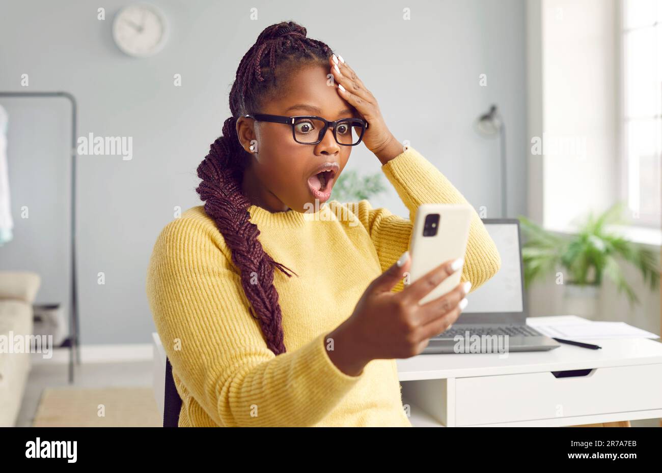 Eine wunderschöne afrikanische Frau sieht vor Schrecken auf das Telefon. Stockfoto