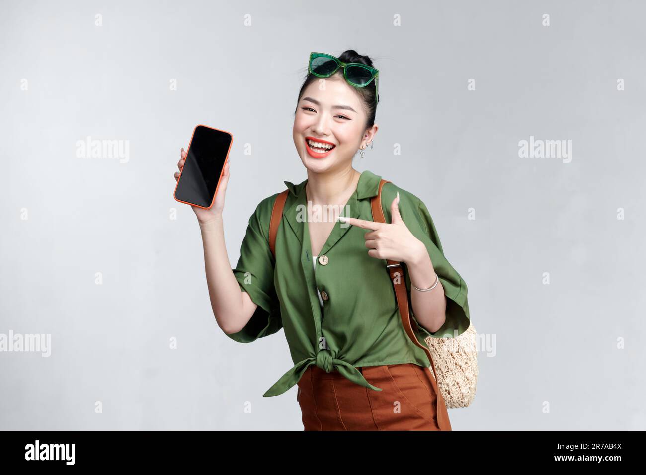 Junge Frau, die ihr Smartphone zeigt, weil sie etwas präsentiert und auf eine Reise im Sommer zeigt Stockfoto