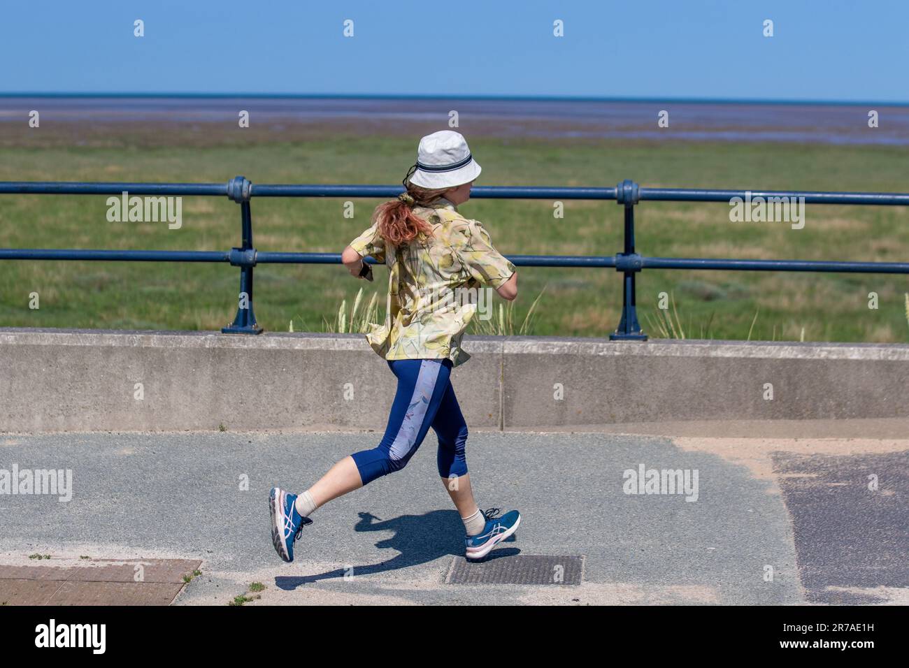 Junge Frau, die in der Sommerhitzewelle in Southport, Merseyside läuft. UK Weather 14. Juni 2023. Stadtratsvernachlässigung im Küstenresort, mit Strandbarrieren, einem Pier, der geschlossen ist, und einer alles andere als verlassenen Promenade und Strandbereich. Stockfoto