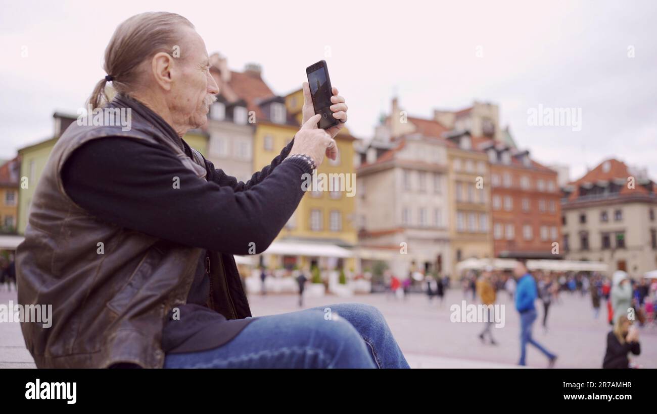 Senior sitzt auf der Treppe und nimmt Sehenswürdigkeiten mit einem Smartphone im historischen Zentrum einer alten europäischen Stadt auf. Palastplatz, Warschauer Altstadt Stockfoto