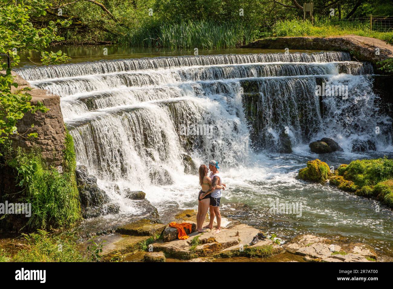 Ein junges Paar umarmte und küsste sich unter einem Wasserfall am Fluss Wye im Monsall Dale Peak District Derbyshire während der Hitzewelle von 2023 Stockfoto
