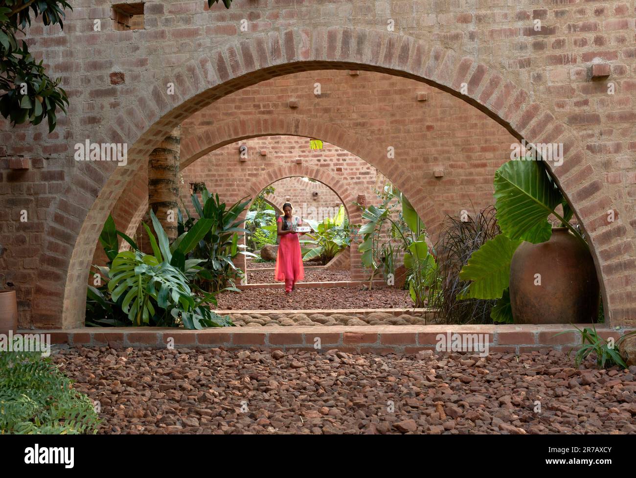 Blick durch Bögen mit Zimmermädchen in farbenfrohem Sari. Subteranische Ruinen, Kaggalipura, Bangalore, Indien. Architekt: A Threshold Architects, 2023. Stockfoto