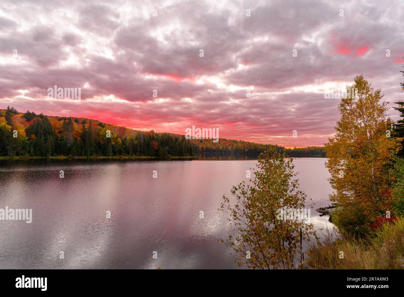 Dramatischer Sonnenuntergang über einem See, umgeben von bewaldeten Hügeln auf dem Gipfel der Herbstfarben Stockfoto