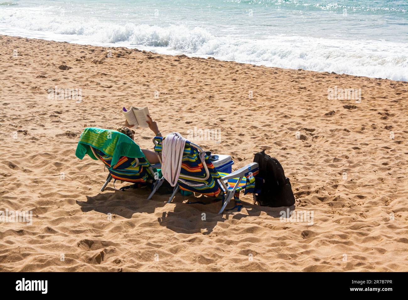 Eine Frau liest am Strand in Los Angeles, Kalifornien, mit Wellen, die auf den Sand in der Nähe prallen Stockfoto
