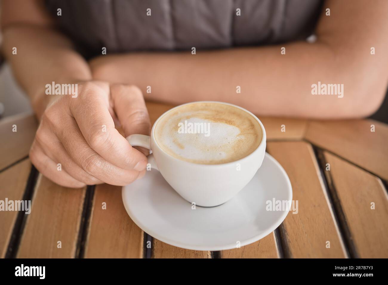 Nahaufnahme einer Tasse duftenden Cappuccino auf dem Tisch in den Händen einer Frau, belebender duftender Kaffee während einer Pause. Selektiver Fokus auf die Finger Stockfoto
