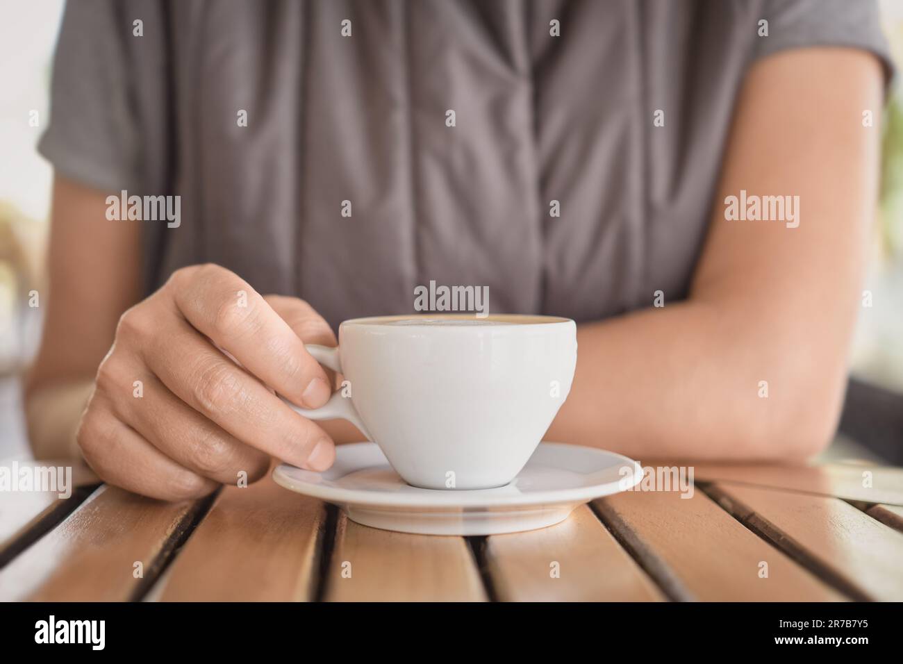 Nahaufnahme einer Tasse Cappuccino oder heißes Getränk und die Hände einer jungen Frau, die während einer Pause Kaffee trinkt. Selektive Fokussierung auf Finger, Idee für Backg Stockfoto