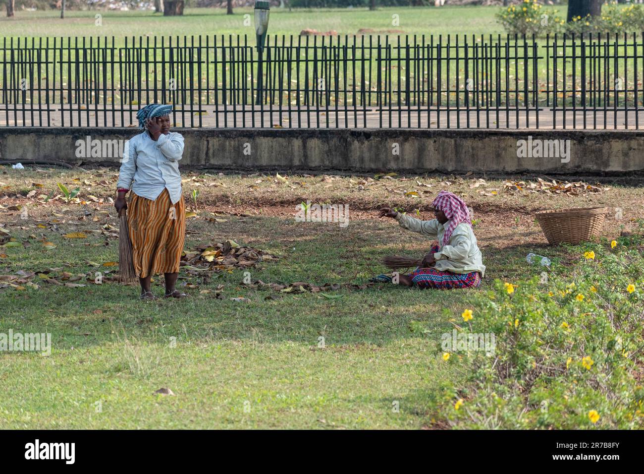 Old Goa, Indien - Januar 2023: Zwei Frauen, die sanitäre Anlagen anfertigen, reinigen den Rasen an der UNESCO-Weltkulturerbestätte Old Goa. Stockfoto