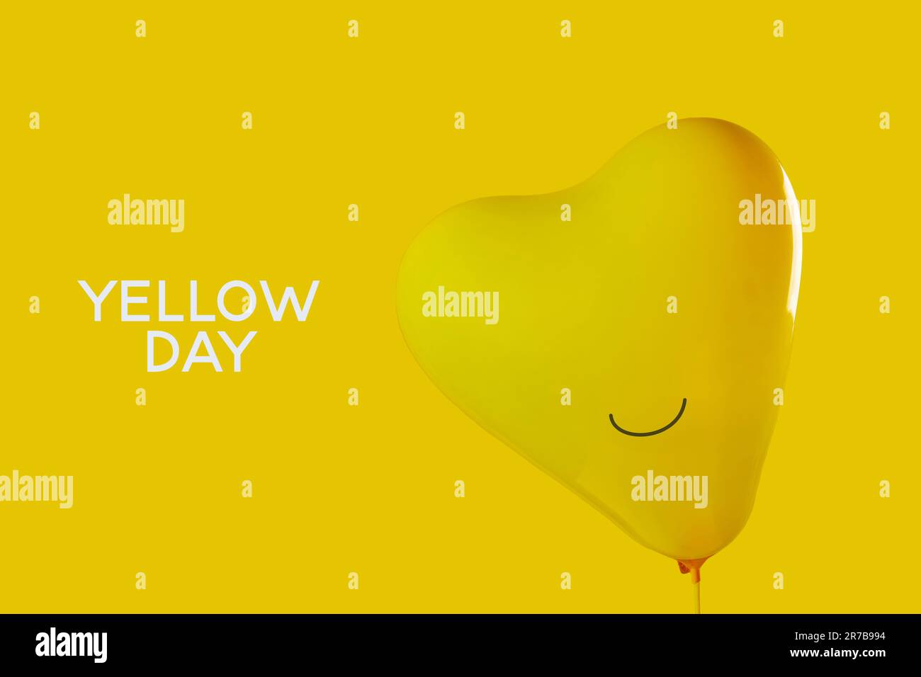 Der Text Gelber Tag und ein aufgeblasener gelber, herzförmiger Ballon mit einem Lächeln auf gelbem Hintergrund Stockfoto