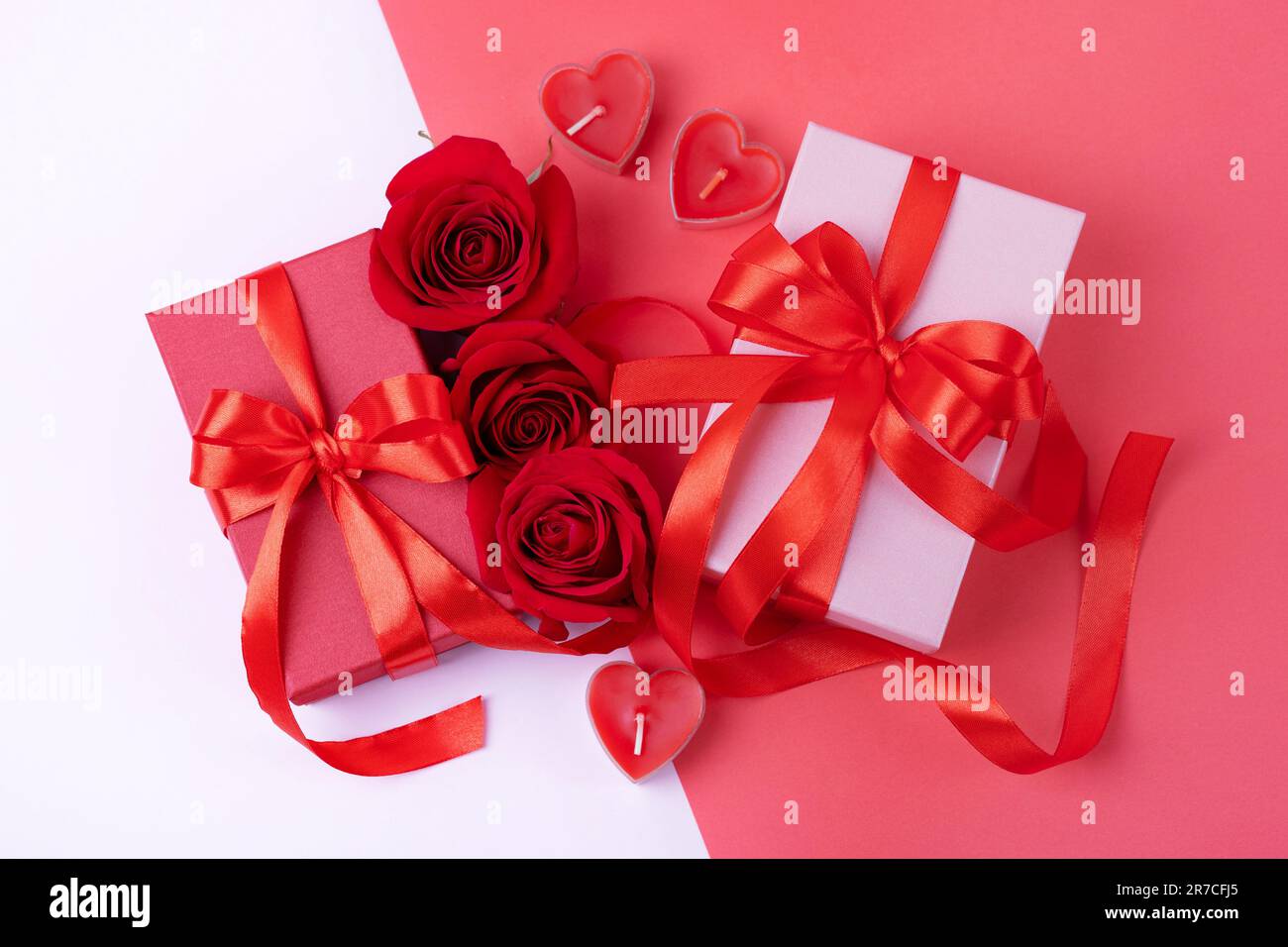 Grußkarte zum Valentinstag, Muttertag und Geburtstag. Rote Rosen, Geschenkschachteln mit einer Schleife aus rotem Satinband auf pinkfarbenem Hintergrund. Draufsicht, flach Stockfoto