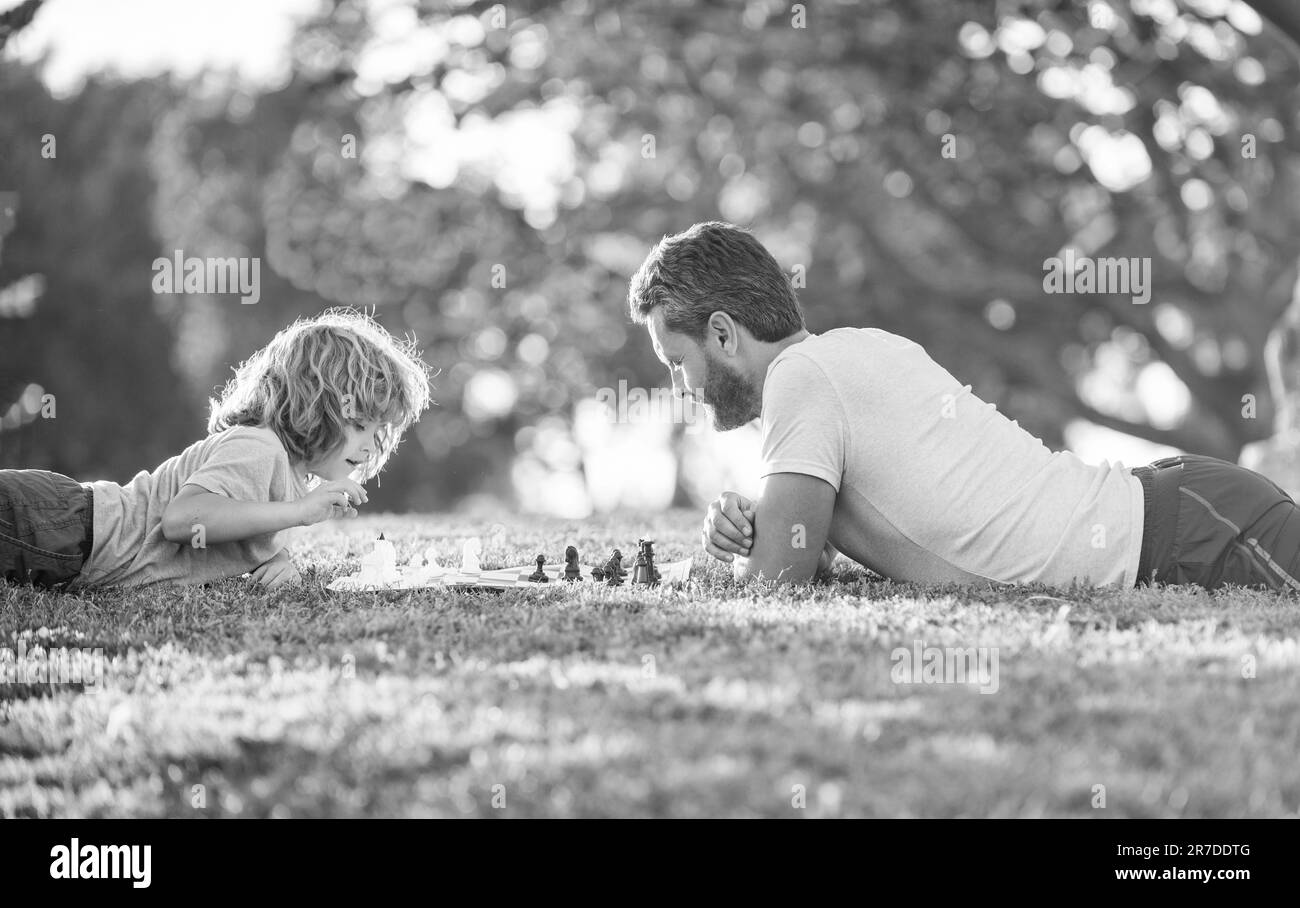 Glückliche Familie von Vater und Sohn Kind spielen Schach auf grünem Gras im Park im Freien, geleckt Stockfoto